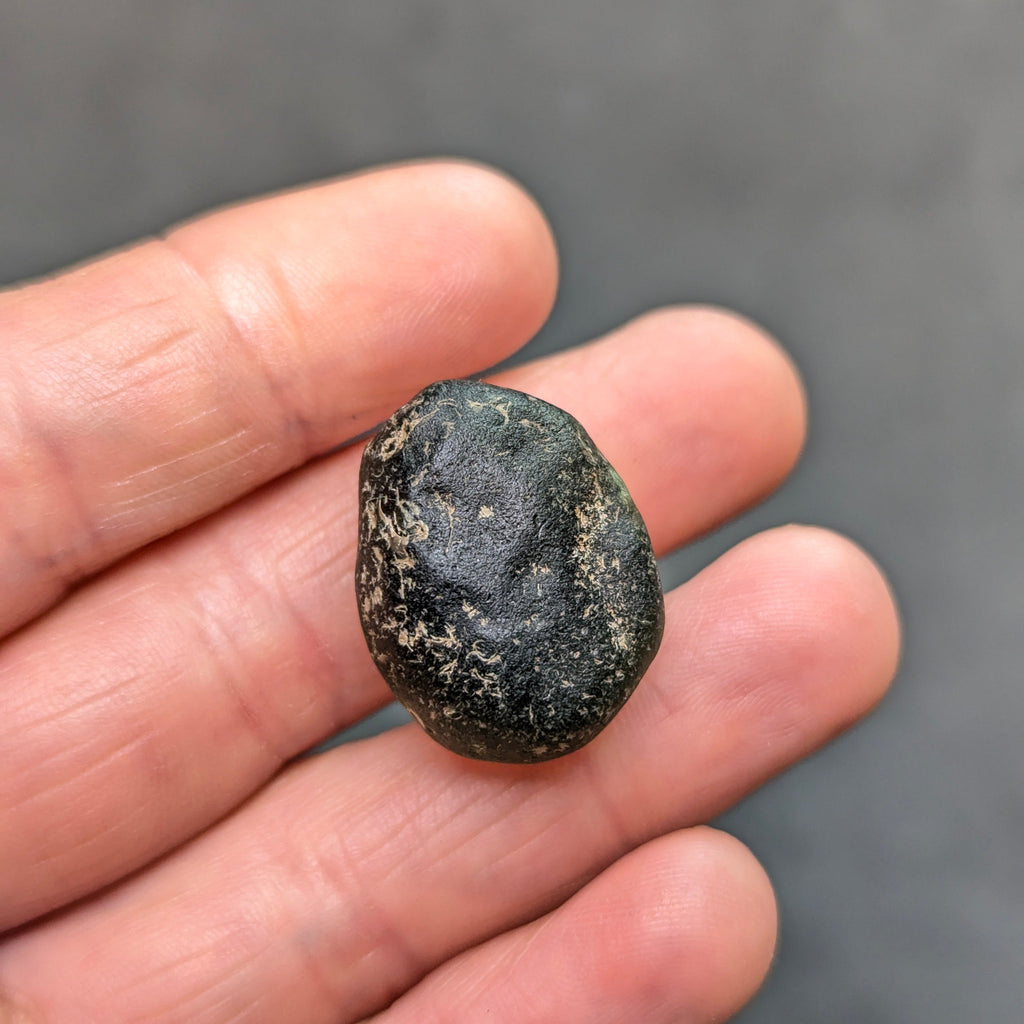 Natural Moldavite from the Zliv locality weighing 7.12 g with rounded oval pebble-like form, naturally worn surface, subtle remaining pits and preserved solid core characteristic of field-found specimens - front view.