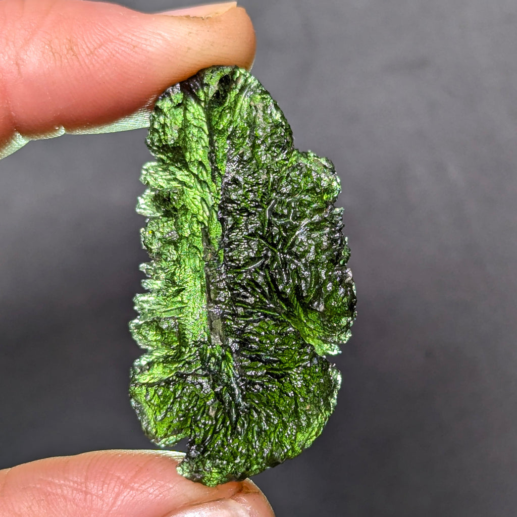 Natural Moldavite from the Olešnice locality weighing 11.82 g with elongated form, deep sharply sculpted texture, pronounced central groove, radiating relief structure and preserved natural surface - front view, backlight.