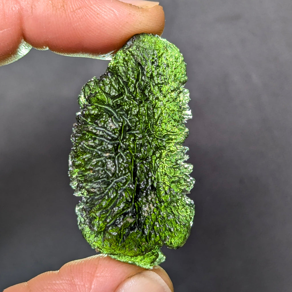 Natural Moldavite from the Olešnice locality weighing 11.82 g with elongated form, deep sharply sculpted texture, pronounced central groove, radiating relief structure and preserved natural surface - back side, backlight.