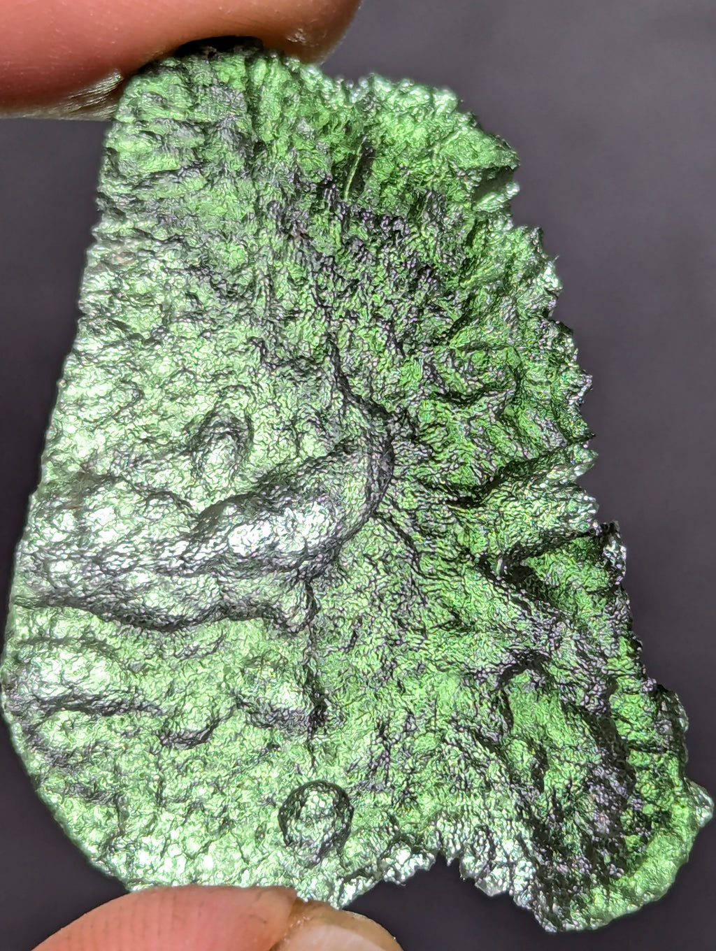 Natural Moldavite from the Olešnice locality weighing 4.69 g with flat elongated shape, sharply sculpted grooves, hammered texture effect and naturally rounded edge in hand - front side, more backlight.