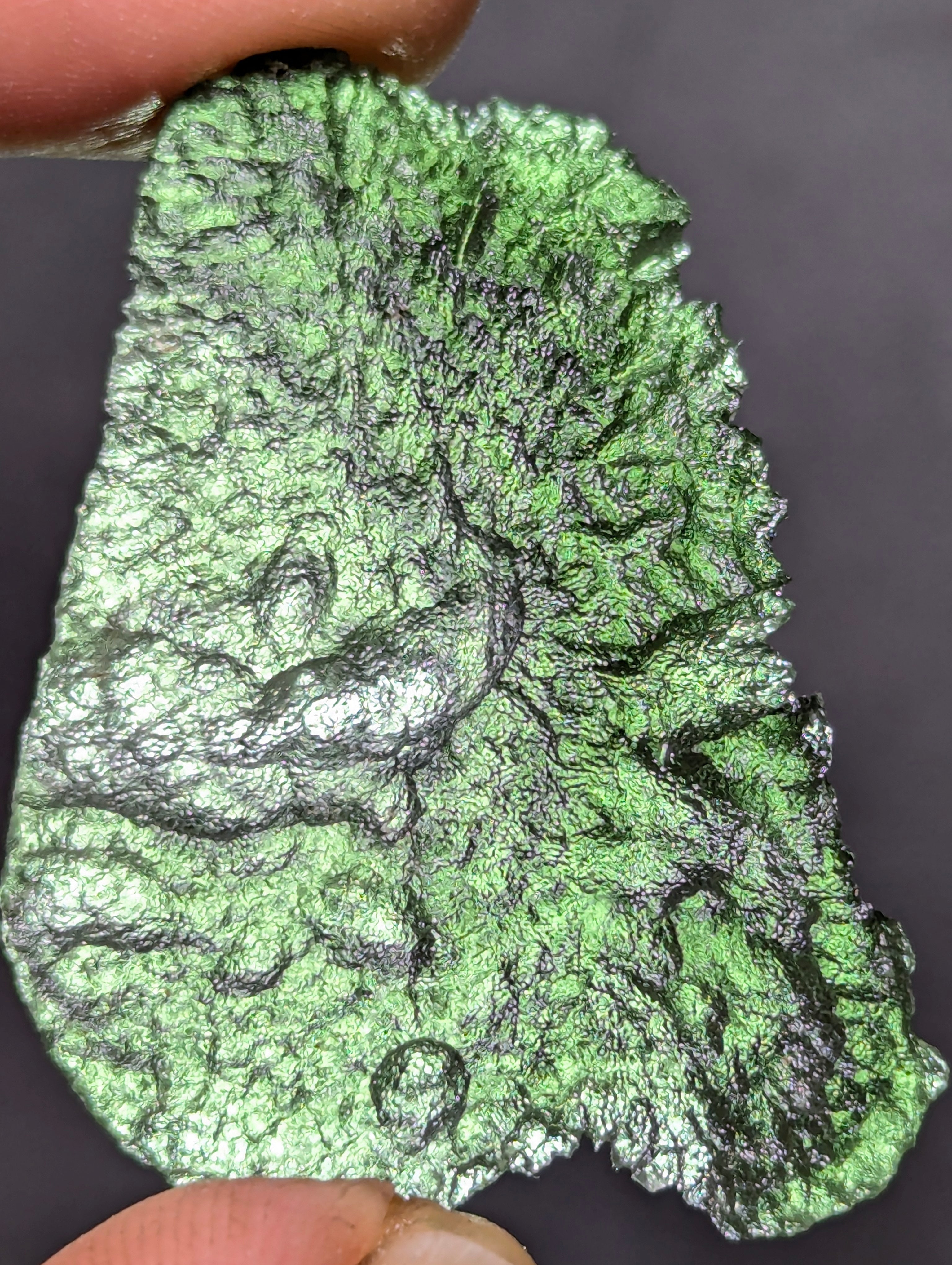 Natural Moldavite from the Olešnice locality weighing 4.69 g with flat elongated shape, sharply sculpted grooves, hammered texture effect and naturally rounded edge in hand - front side, more backlight.
