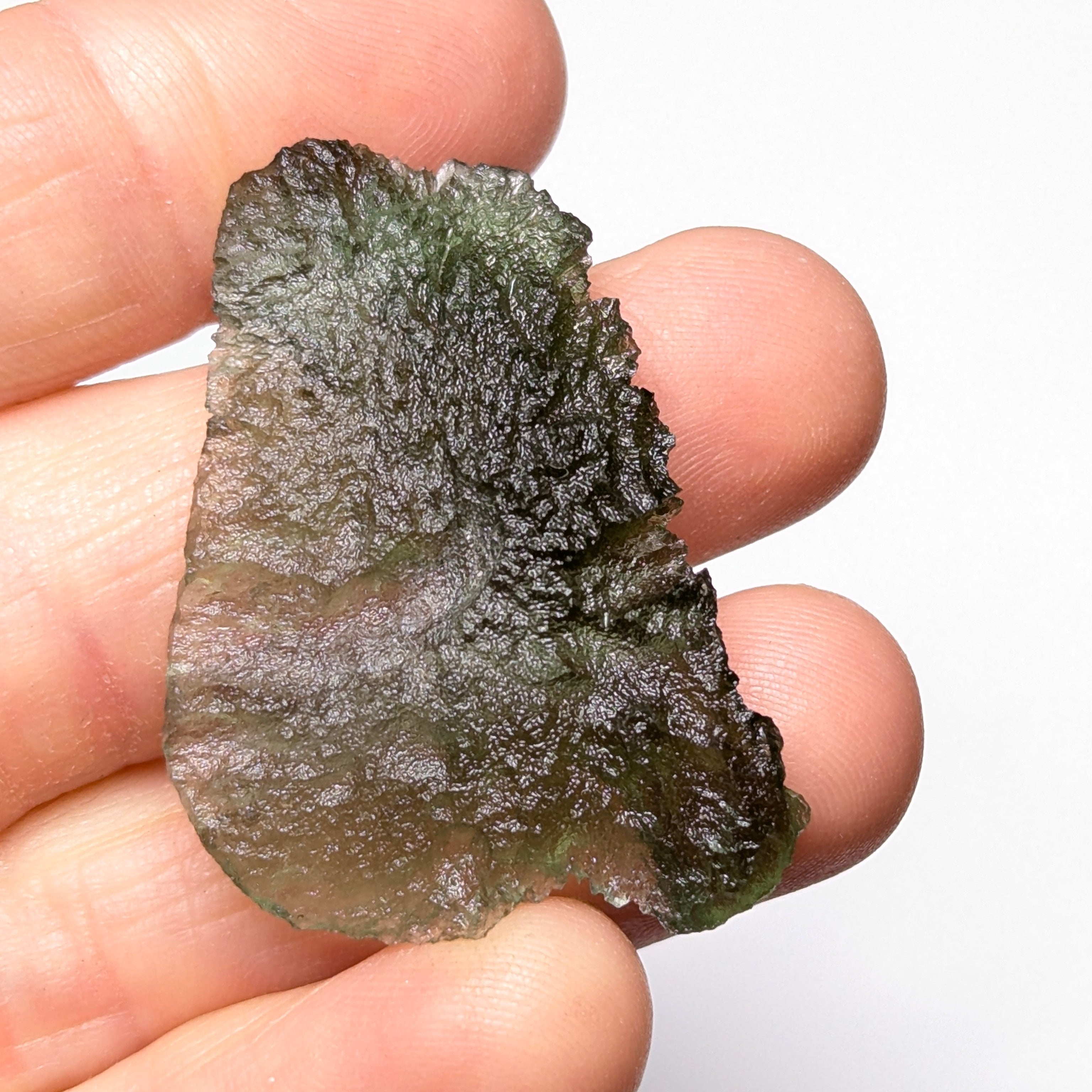 Natural Moldavite from the Olešnice locality weighing 4.69 g with flat elongated shape, sharply sculpted grooves, hammered texture effect and naturally rounded edge in hand - front side.