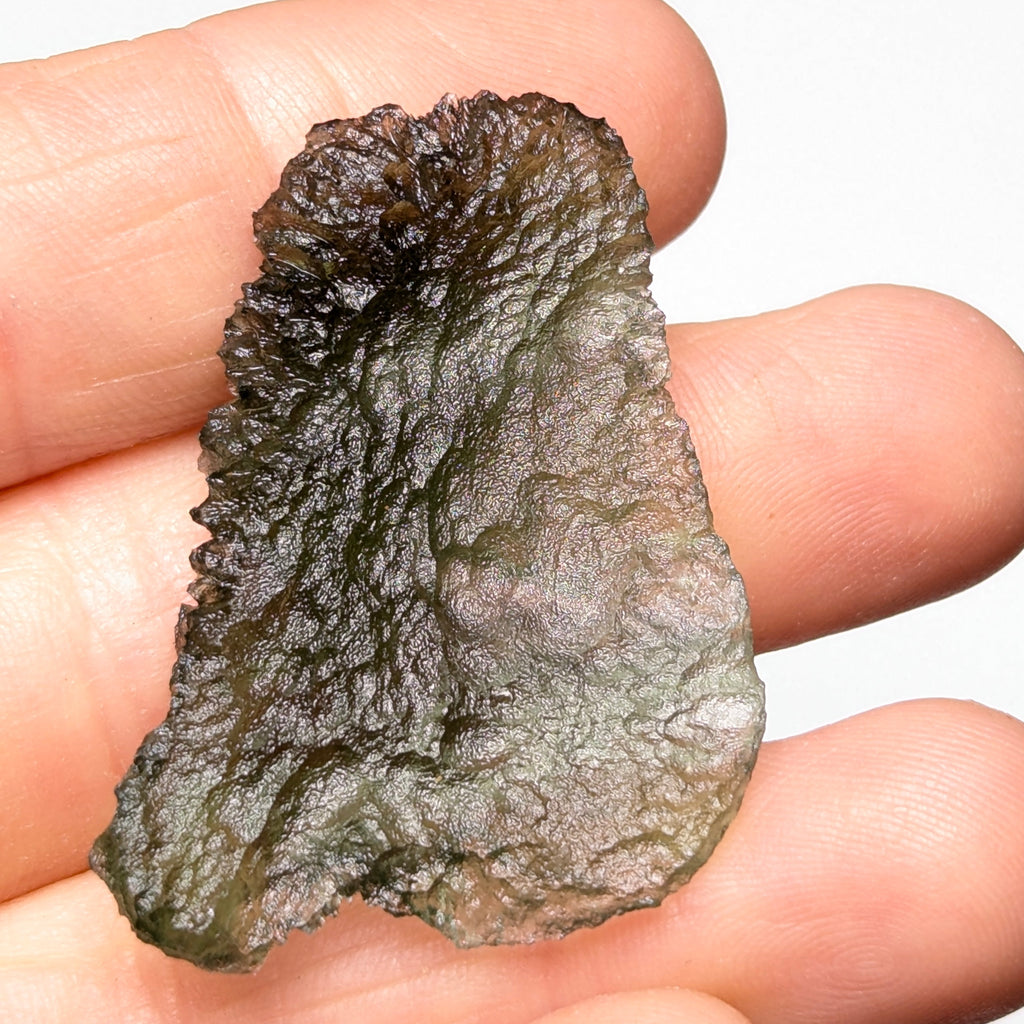 Natural Moldavite from the Olešnice locality weighing 4.69 g with flat elongated shape, sharply sculpted grooves, hammered texture effect and naturally rounded edge in hand - back side.