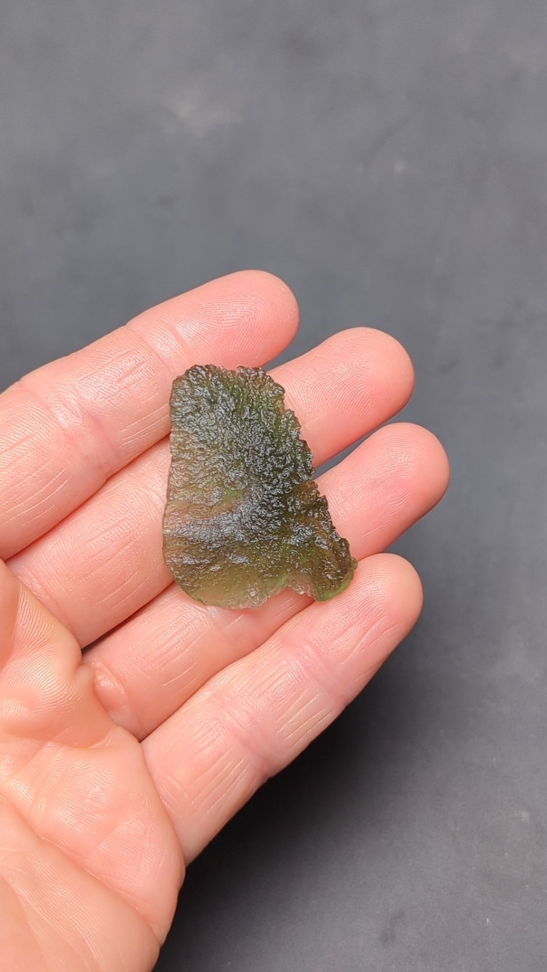 Natural Moldavite from the Olešnice locality weighing 4.69 g with flat elongated shape, sharply sculpted grooves, hammered texture effect and naturally rounded edge in hand - video.