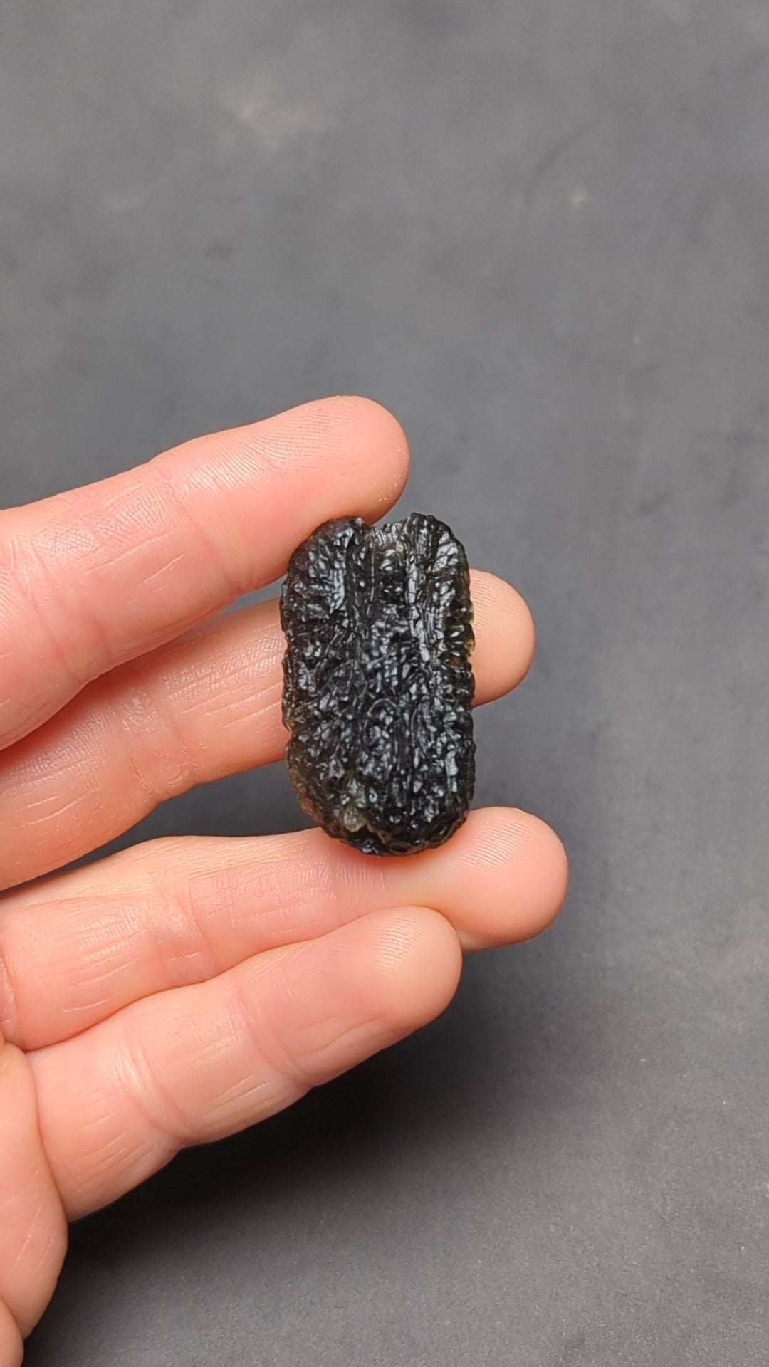 Natural Moldavite from the Olešnice locality with dramatic sculpture, deep central groove, naturally opened bubbles and vivid green translucency under illumination in hand - video.