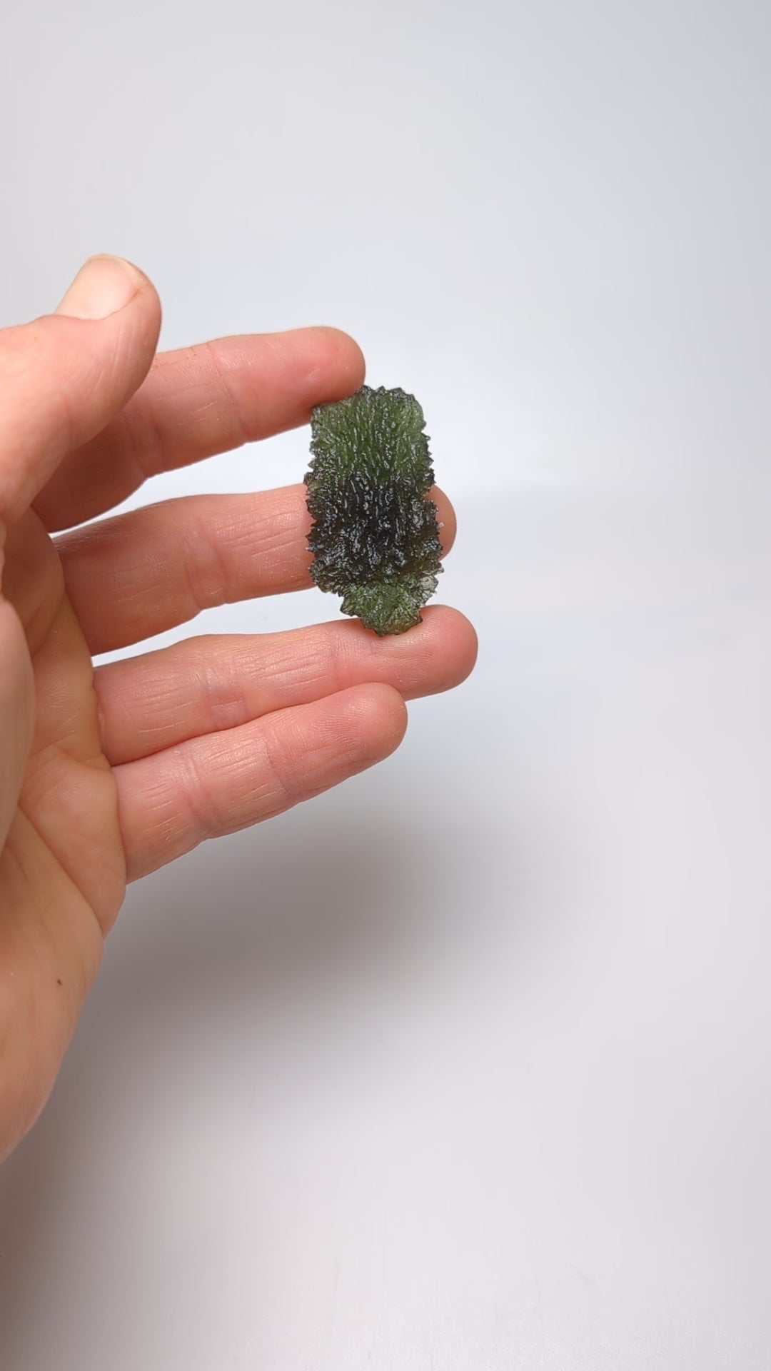 Natural Moldavite from the Dobrovská Lhotka – Bažina locality with rich sculpture, serrated edges, saturated olive green color and pronounced surface texture in hand - video.
