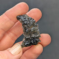 Rare “angel chime” Moldavite from the Olešnice locality in hand with thin hollow structure, sharp radial sculpture, golden green translucency and pointed natural relief - front view.