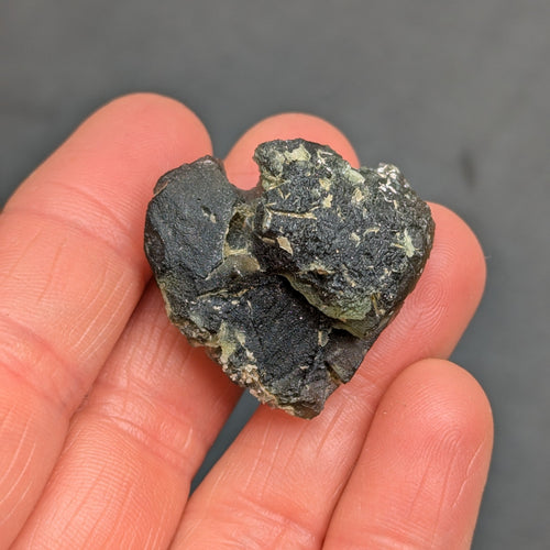 Heart-shaped natural raw moldavite with newly formed sculpture after natural separation, velvety matte surface and fine pyramidal micro-sculpture in hand - front view.
