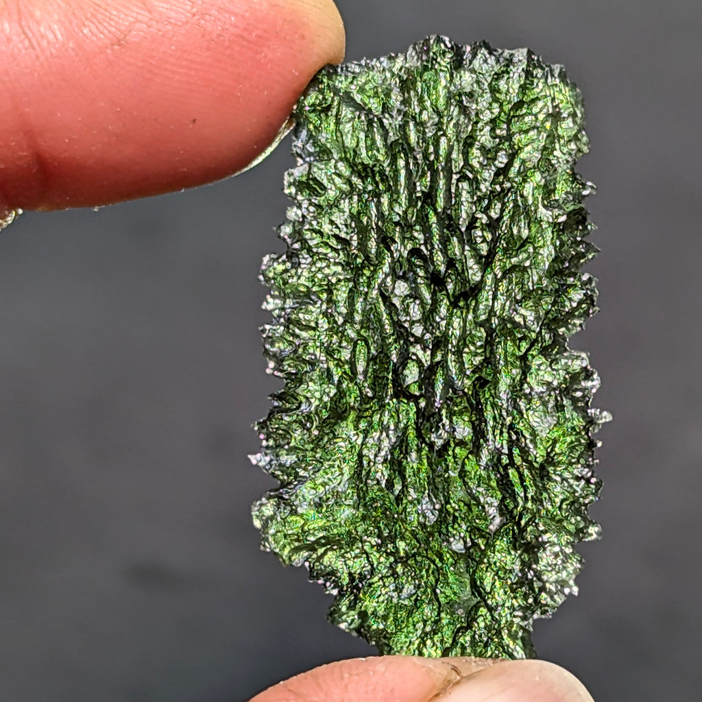 Natural Moldavite from the Dobrovská Lhotka – Bažina locality with rich sculpture, serrated edges, saturated olive green color and pronounced surface texture in hand - front view, backlight.