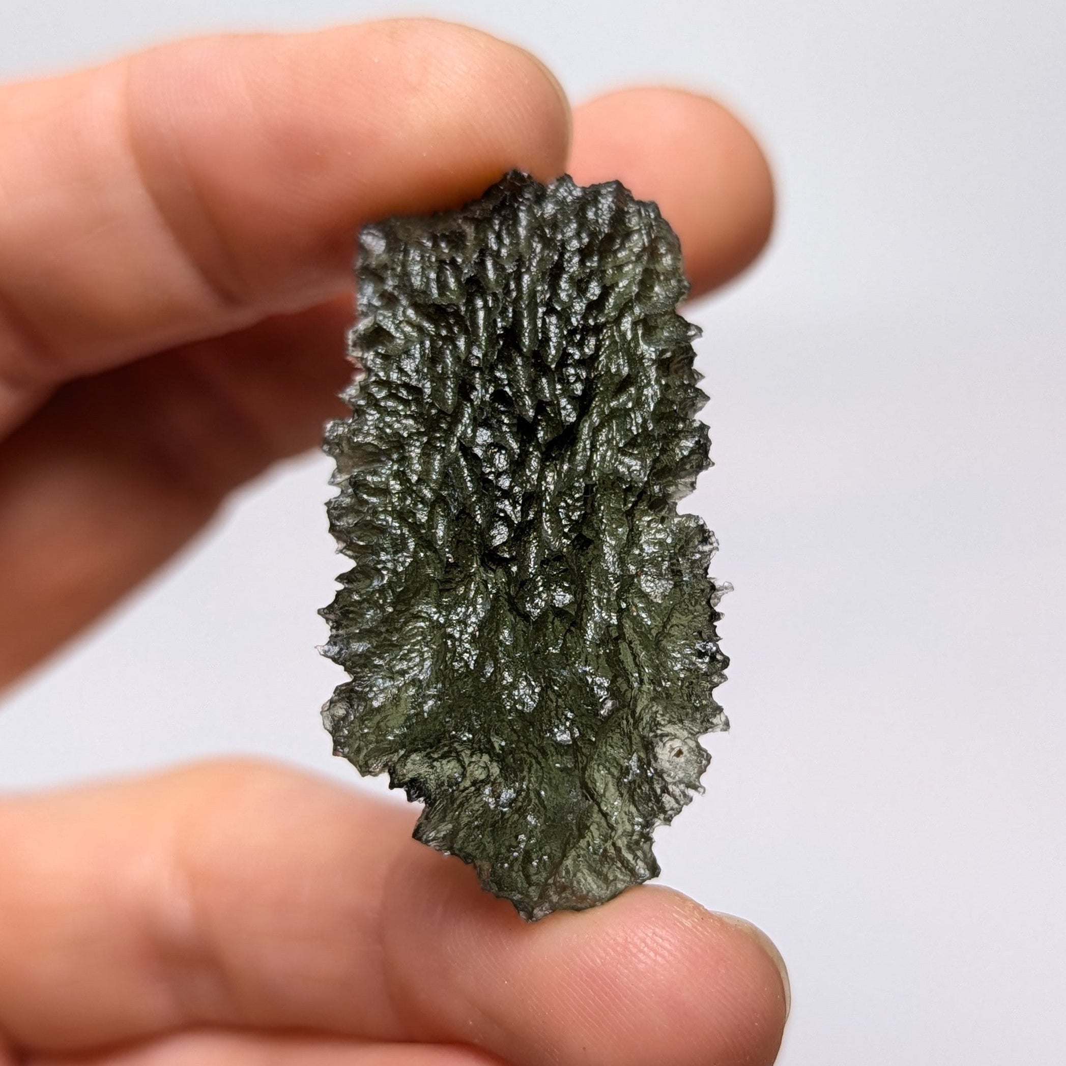 Natural Moldavite from the Dobrovská Lhotka – Bažina locality with rich sculpture, serrated edges, saturated olive green color and pronounced surface texture in hand - front view.