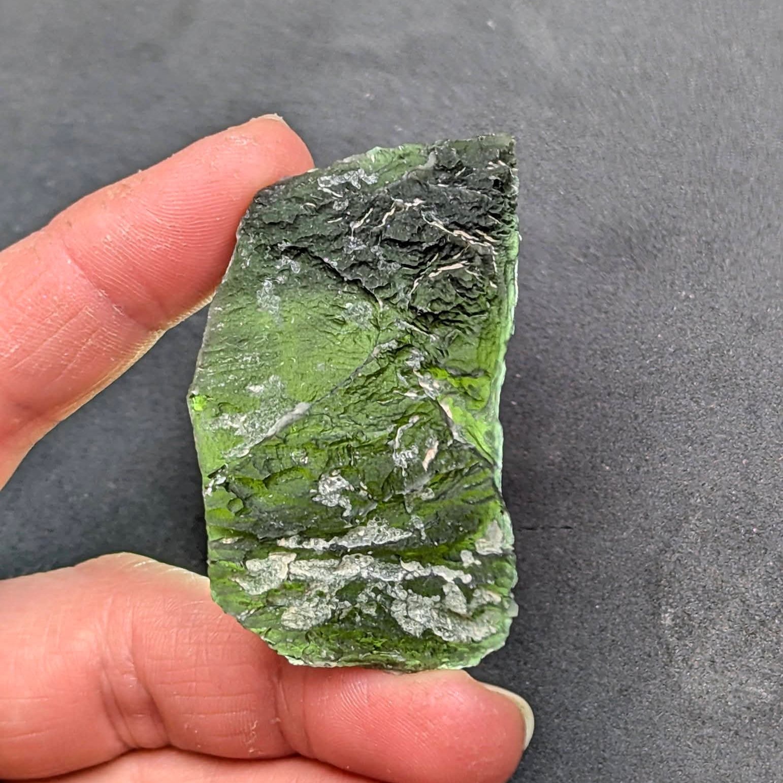Natural Slavče 25.71 g moldavite with two different sculpting textures and elongated natural shape - front view, backlight.