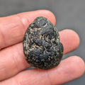 Olive green moldavite 12.5g from Zliv, oval shape with clay residues, front view, in hand.