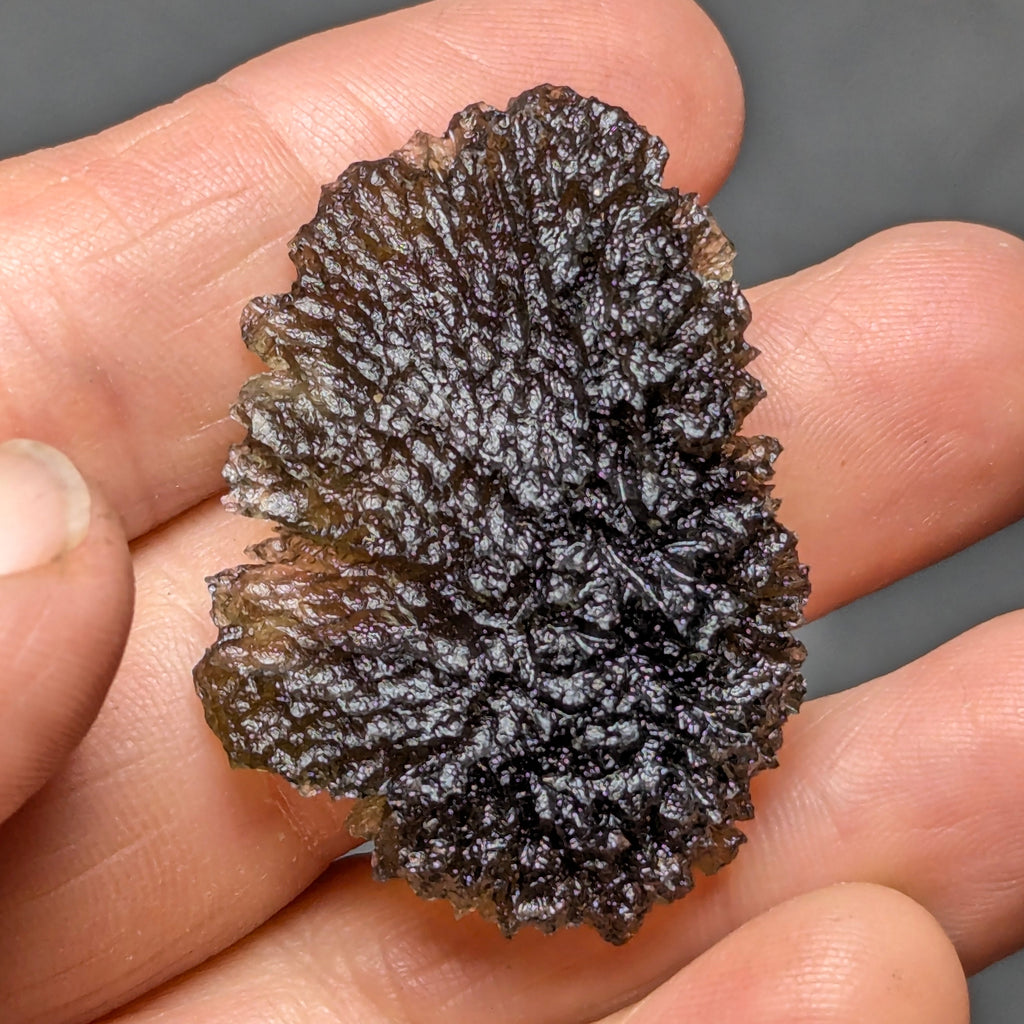 Natural Moldavite from the Olešnice locality with deep sharply sculpted texture, pronounced grooves, complex relief and contrasting green translucency in hand - front view.