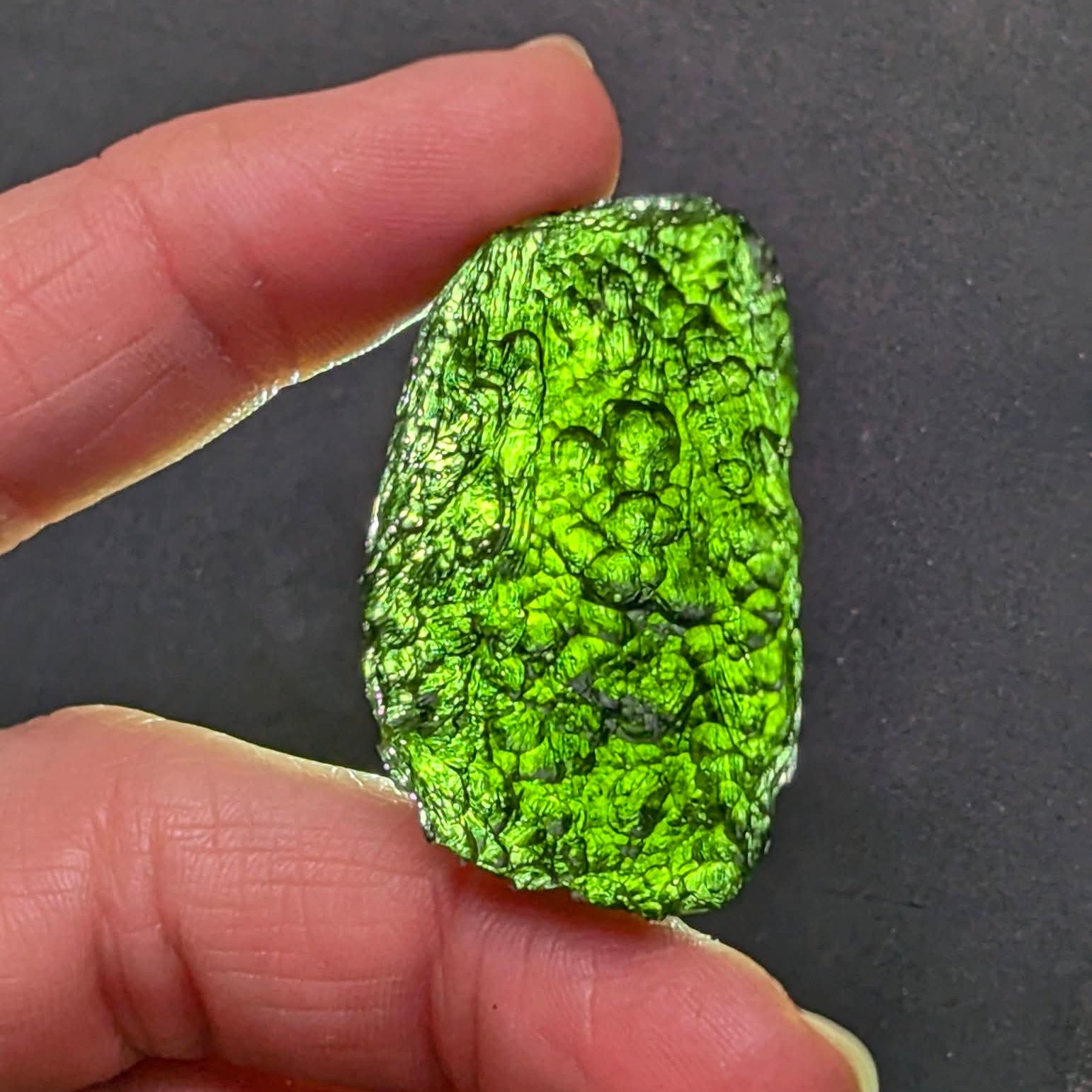 Natural Moldavite from the Krasejovka locality on white background with glossy lacquer-like surface, deep sculpture, pronounced grooves, vivid green translucency and authentic natural relief. Weight 14 g - front view, backlight.