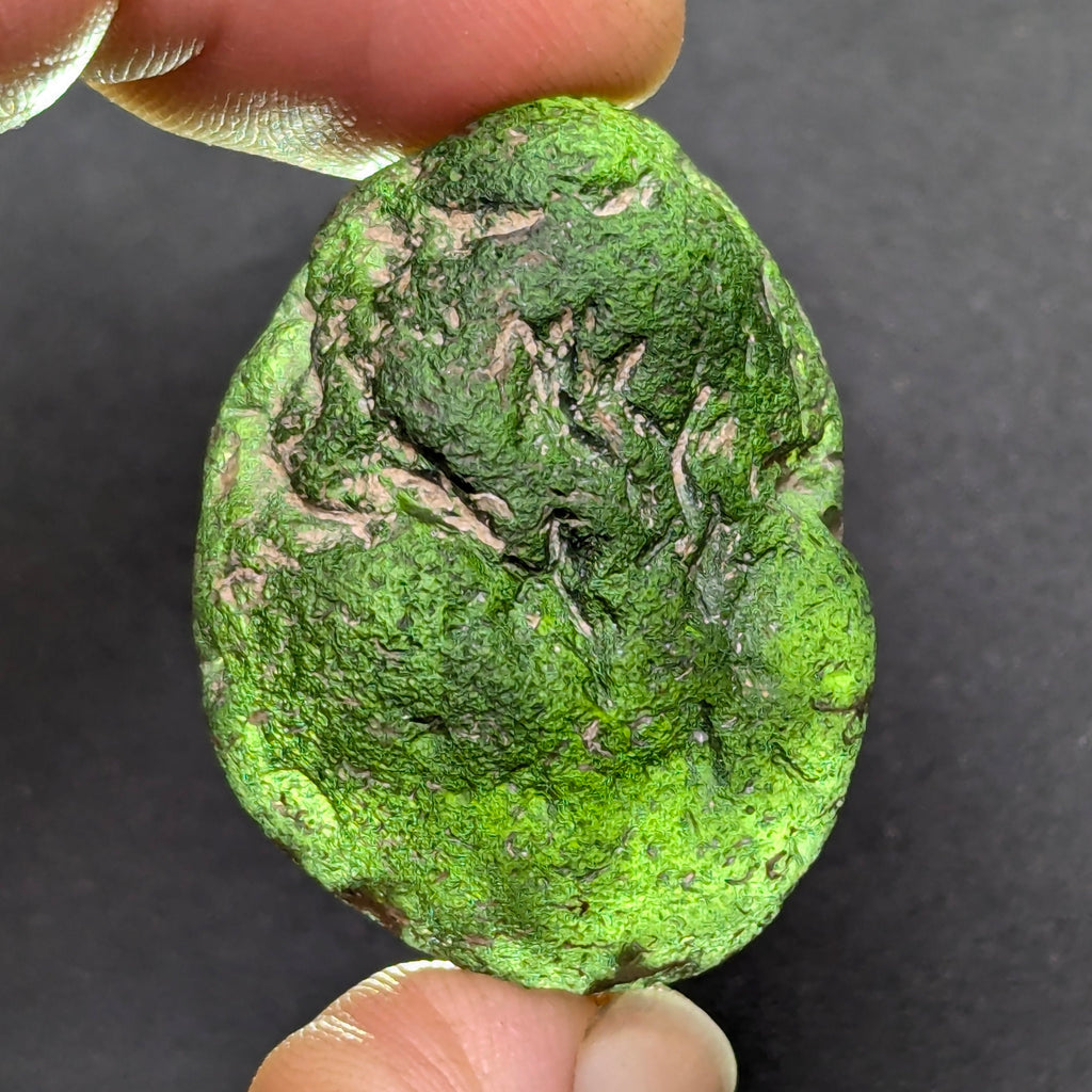 Olive green moldavite 12.5g from Zliv, oval shape with clay residues, front view, backlight.