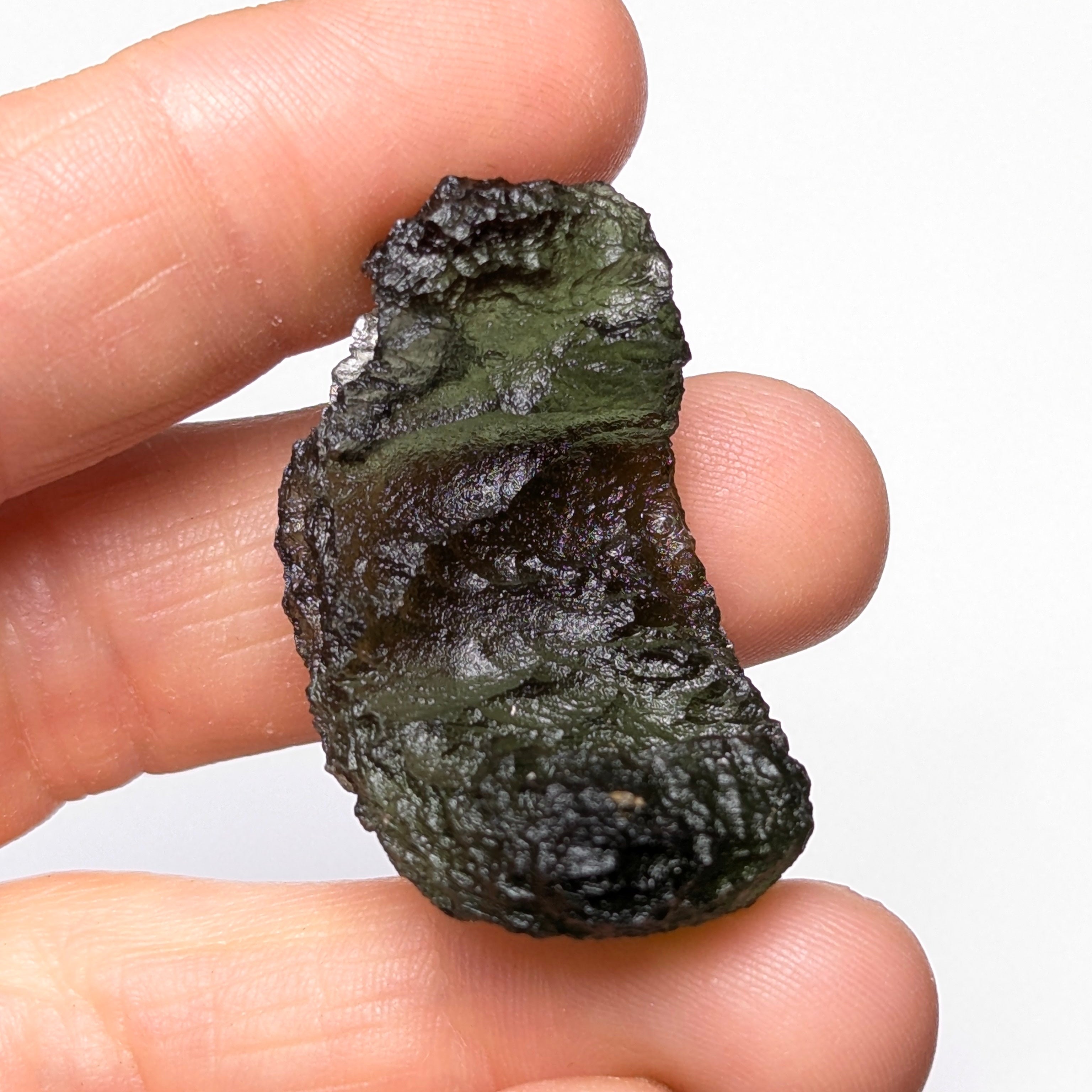 Natural Moldavite from the Olešnice locality weighing 8.86 g with hollow shape, open bubble formation, matte to velvety surface, subtle glossy areas and olive green color in hand - back view.