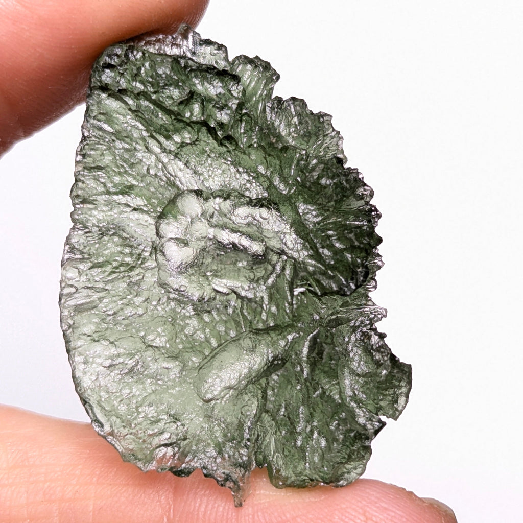 Natural Moldavite from the Olešnice locality with electrifying neon green color, glossy luster, deep grooves and vivid green translucency under illumination in hand - back view.