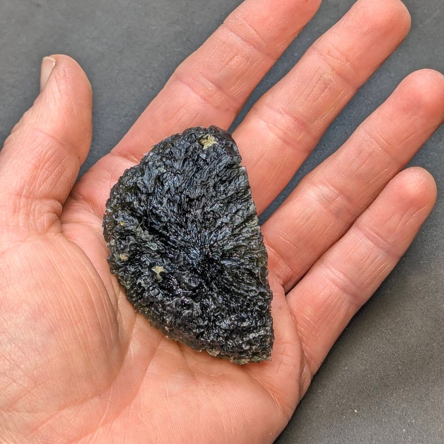 Natural moldavite from Krasejovka, 41 g half-disc - front view, in hand.