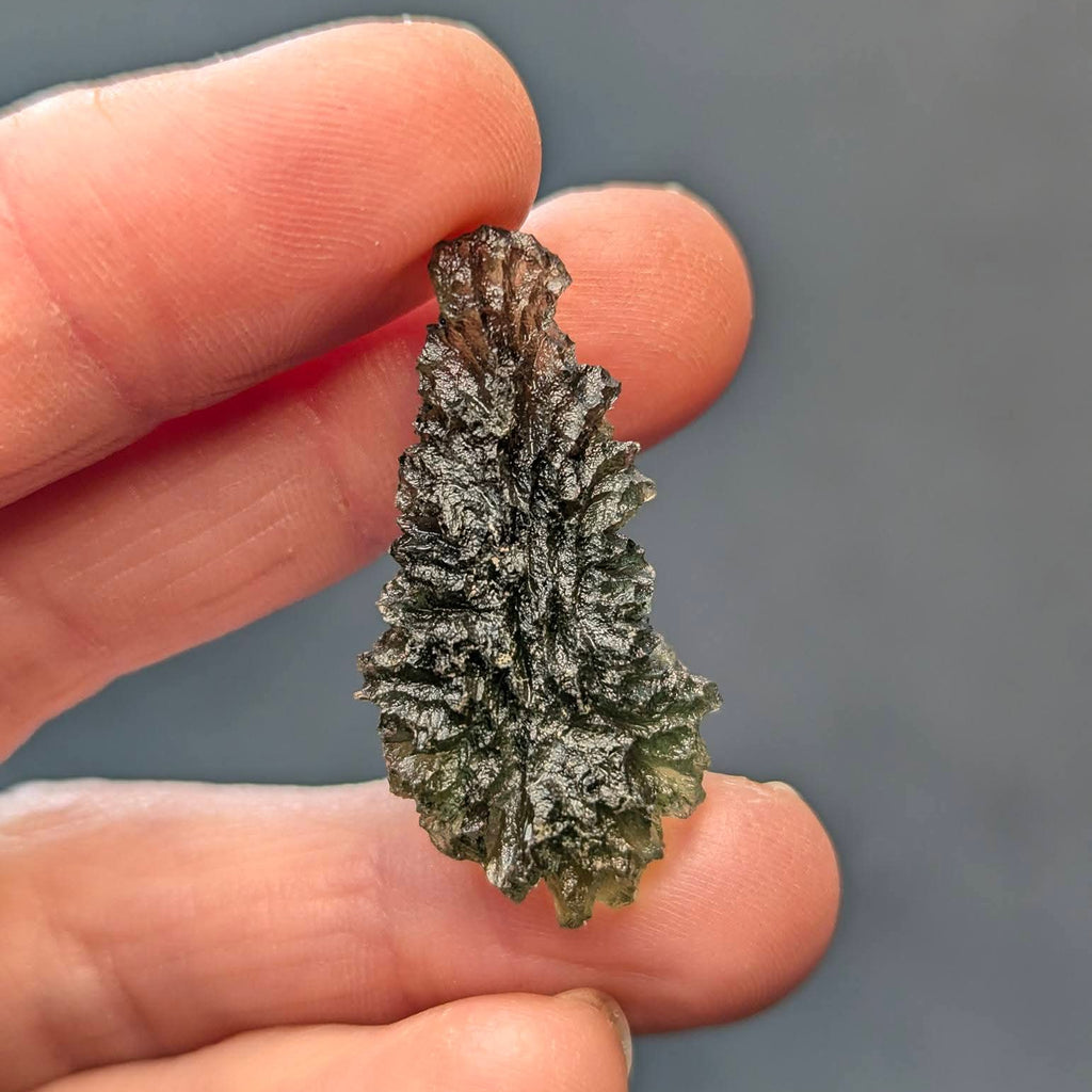 Natural raw teardrop-shaped Olešnice moldavite with pronounced deep sculpture and authentic surface texture - back view.