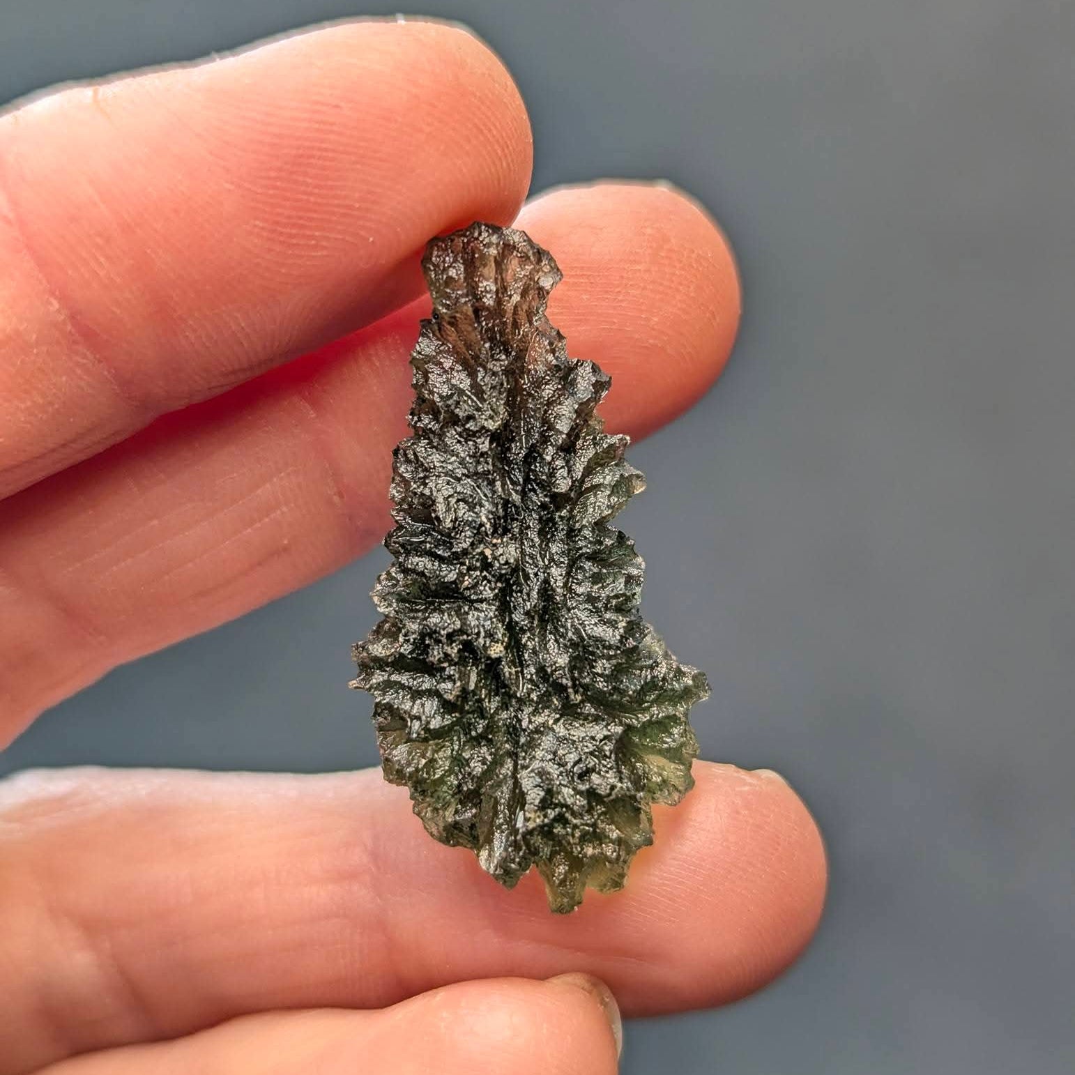 Natural raw teardrop-shaped Olešnice moldavite with pronounced deep sculpture and authentic surface texture - back view.