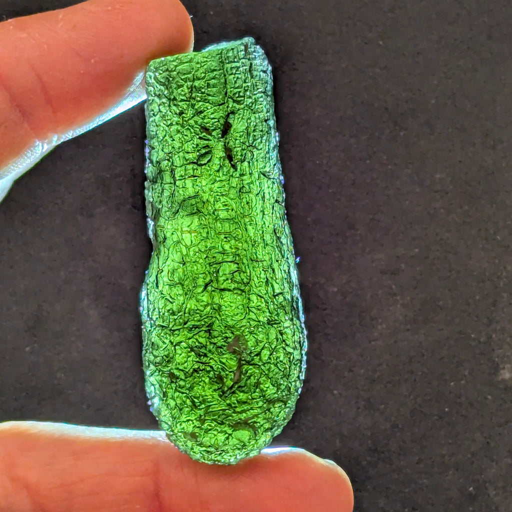 Natural Moldavite from the Jankov locality in hand, front view with elongated drop-like shape, tree bark sculpture, dark olive green translucency and authentic natural relief. Weight 15.62 g - front view, backlight.