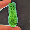 Natural Moldavite from the Jankov locality in hand, front view with elongated drop-like shape, tree bark sculpture, dark olive green translucency and authentic natural relief. Weight 15.62 g - front view, backlight.