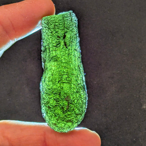 Natural Moldavite from the Jankov locality in hand, front view with elongated drop-like shape, tree bark sculpture, dark olive green translucency and authentic natural relief. Weight 15.62 g - front view, backlight.