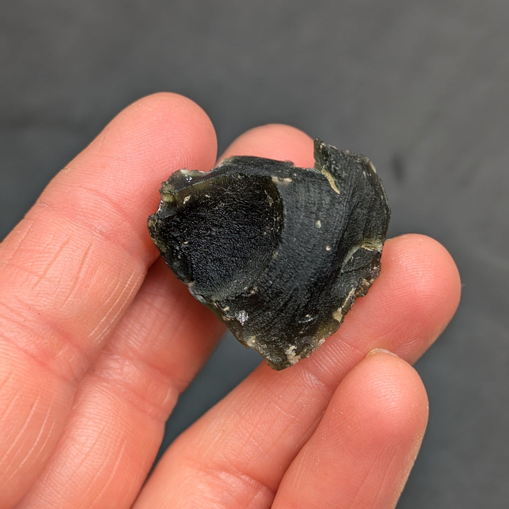 Heart-shaped natural raw moldavite with newly formed sculpture after natural separation, velvety matte surface and fine pyramidal micro-sculpture in hand - back side.