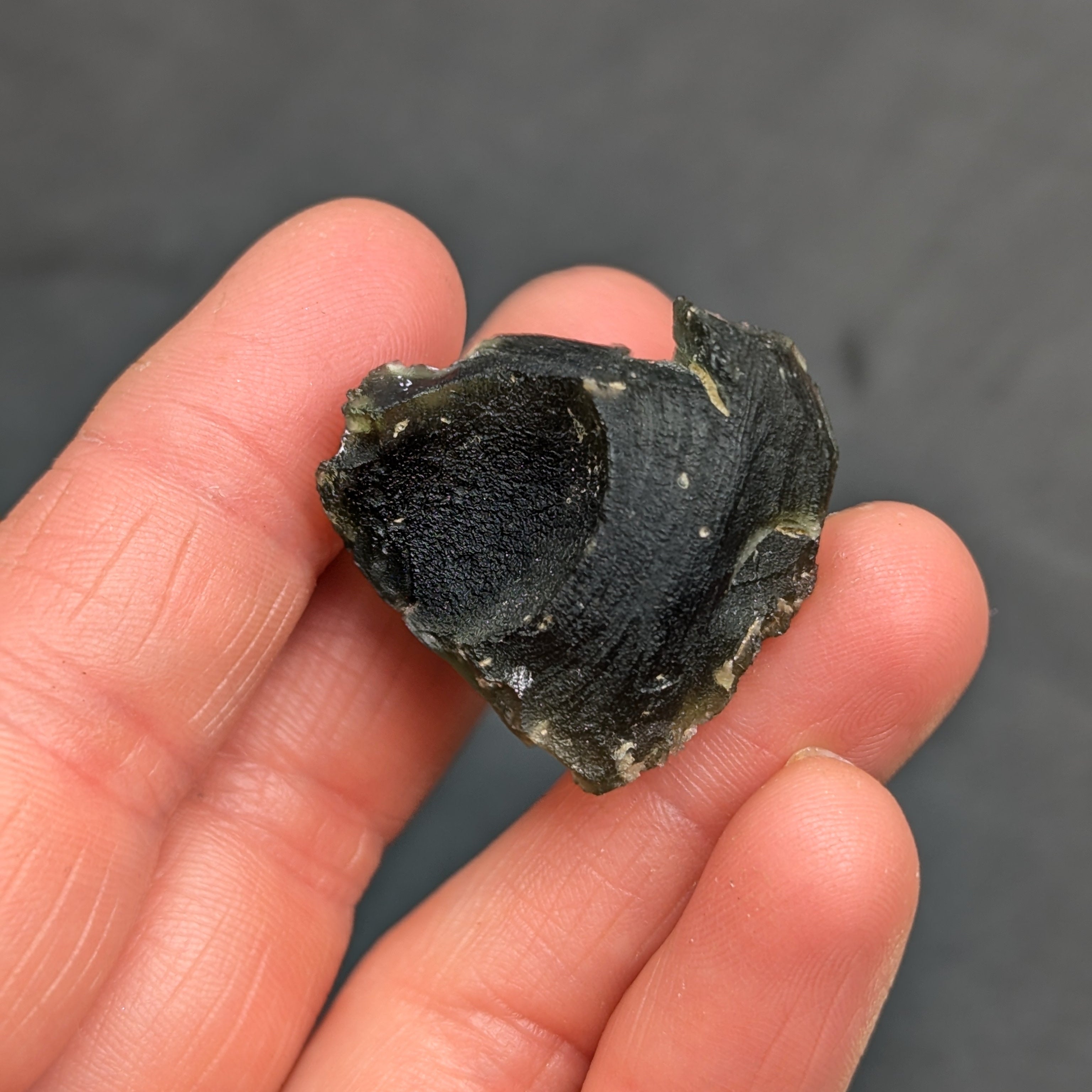 Heart-shaped natural raw moldavite with newly formed sculpture after natural separation, velvety matte surface and fine pyramidal micro-sculpture in hand - back side.