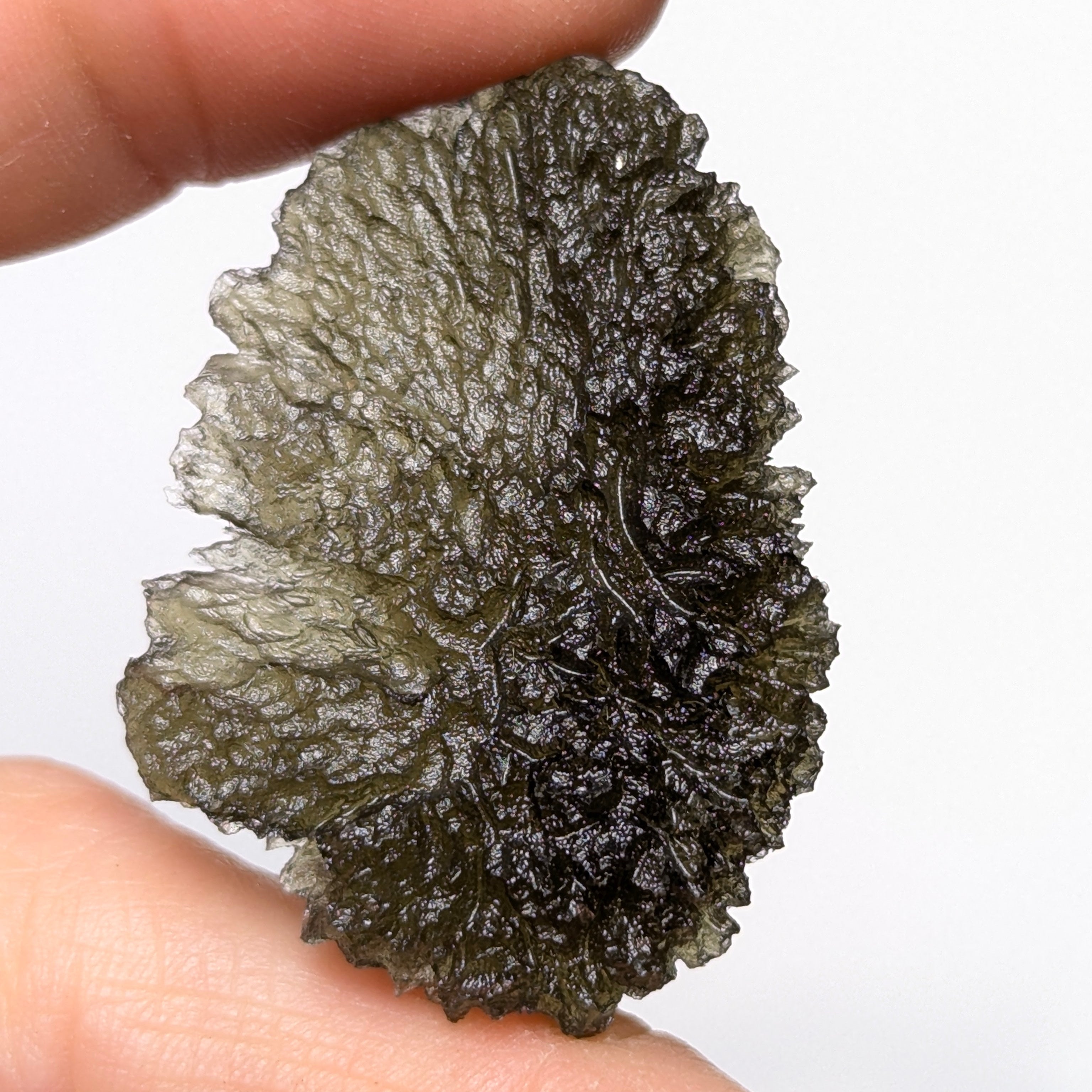 Natural Moldavite from the Olešnice locality with deep sharply sculpted texture, pronounced grooves, complex relief and contrasting green translucency in hand - front side.