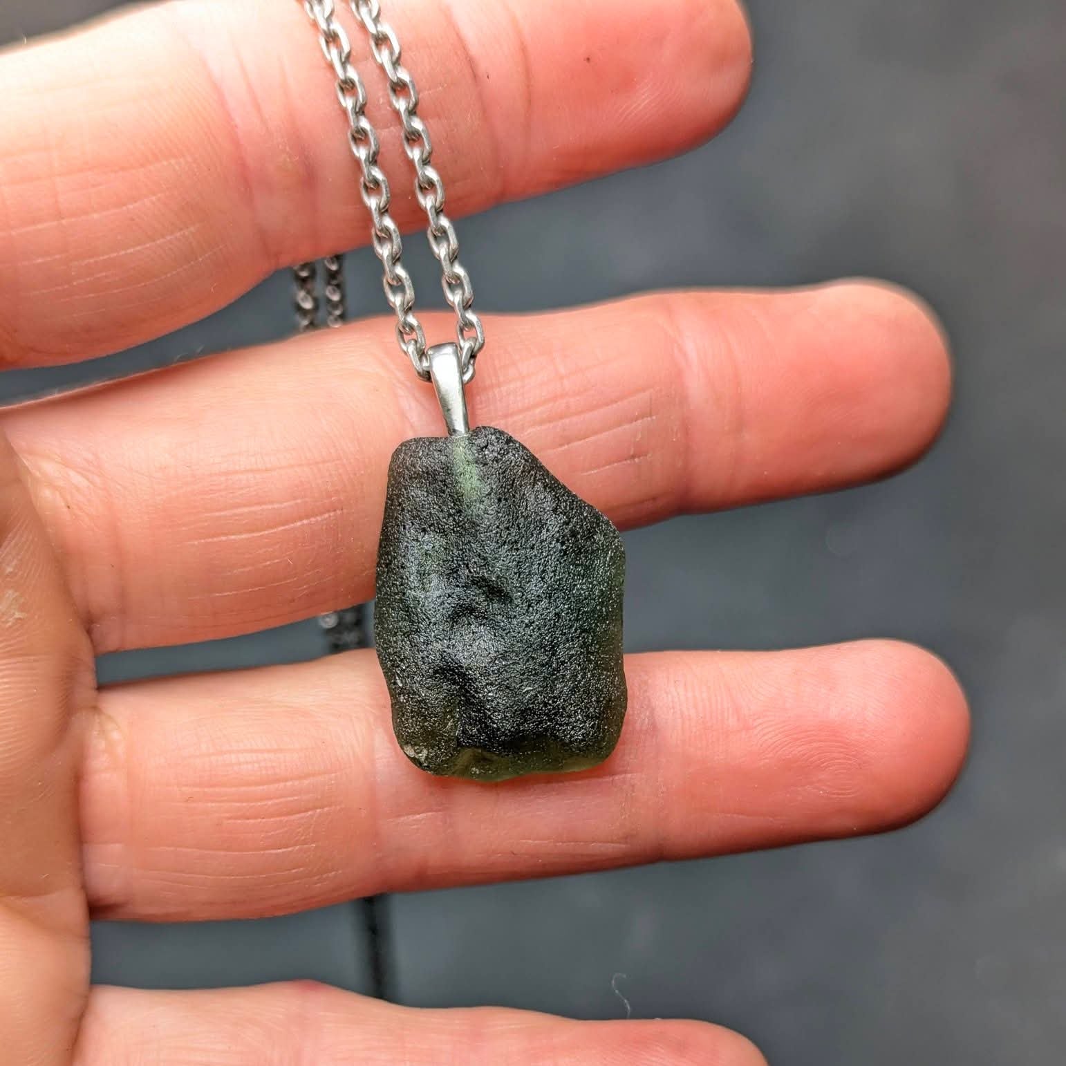 Natural Radomilice 4 g moldavite pendant with Ag 925 silver bail, light yellow-green color and naturally rounded sculpted surface - front side, in hand.