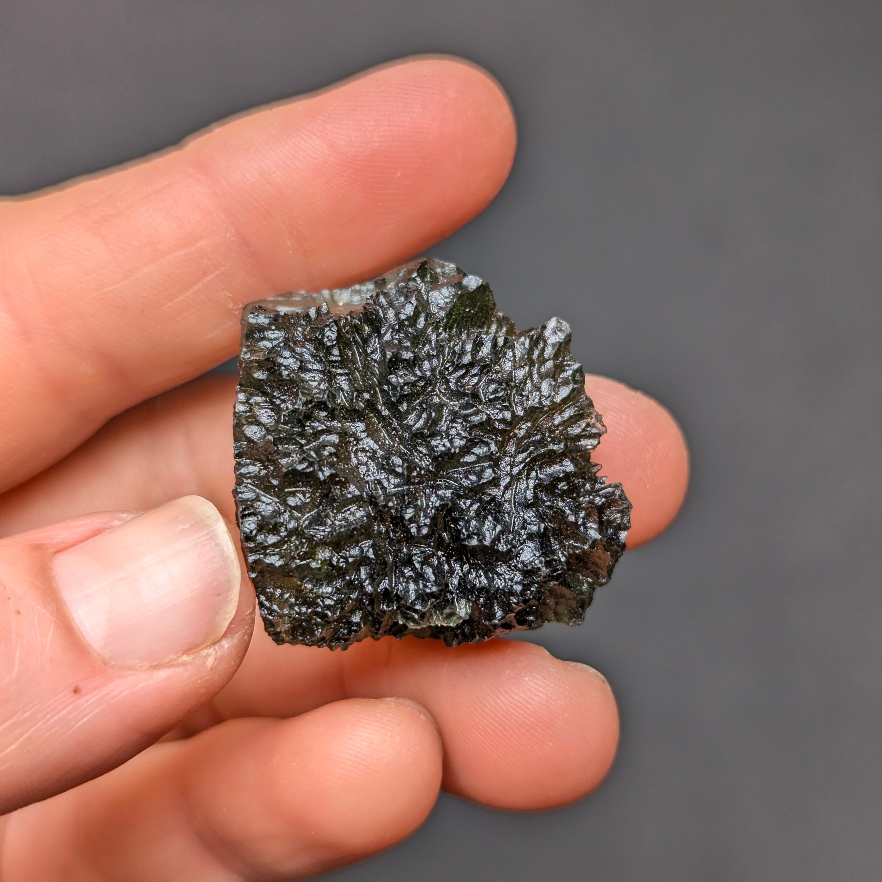 Natural Olešnice 13.87 g moldavite with deep sculpted texture and vivid green translucency under transmitted light - front view.