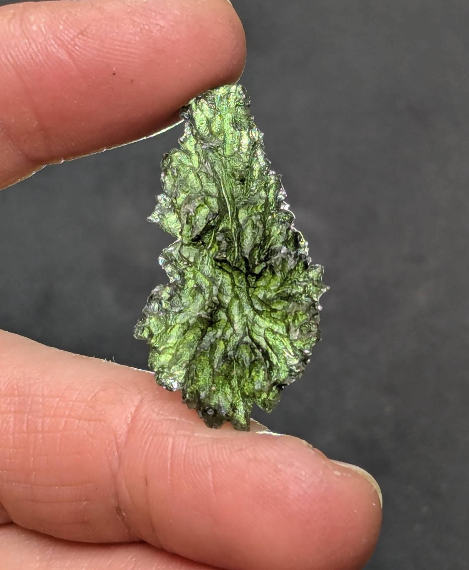 Natural raw teardrop-shaped Olešnice moldavite with pronounced deep sculpture and authentic surface texture - front view, backlight.