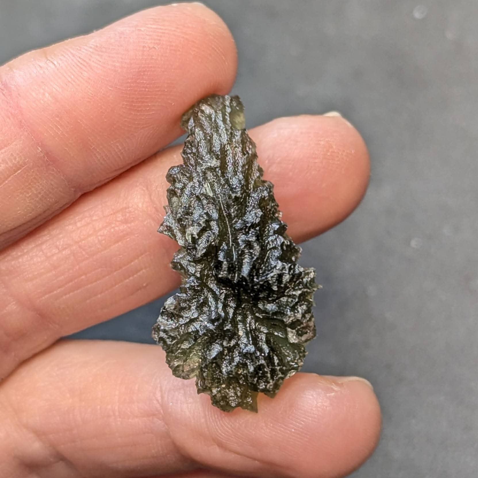 Natural raw teardrop-shaped Olešnice moldavite with pronounced deep sculpture and authentic surface texture - front view.