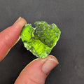 Heart-shaped natural raw moldavite with newly formed sculpture after natural separation, velvety matte surface and fine pyramidal micro-sculpture in hand - front view, backlight.
