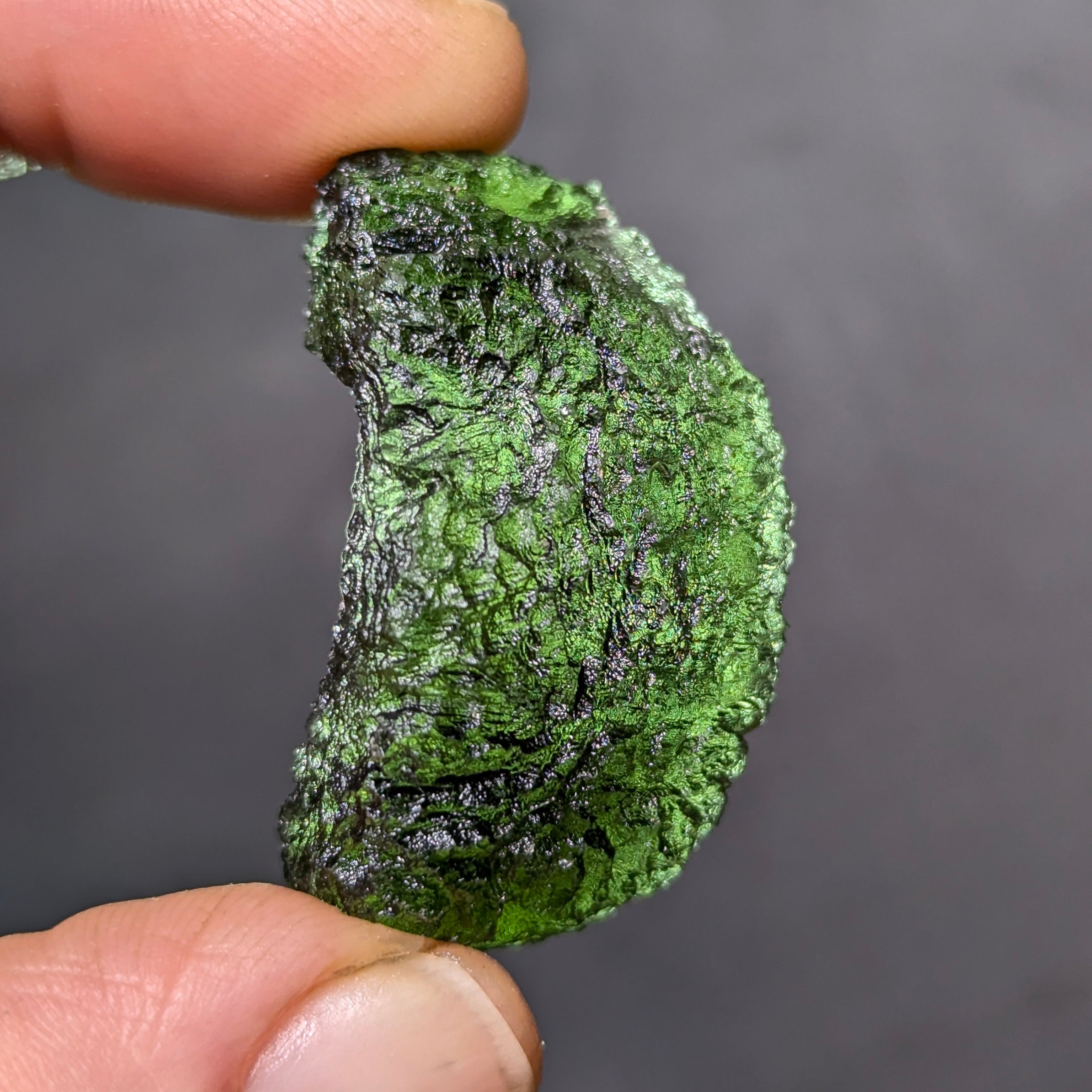 Natural Moldavite from the Olešnice locality weighing 8.86 g with hollow shape, open bubble formation, matte to velvety surface, subtle glossy areas and olive green color in hand - side view, backlight.