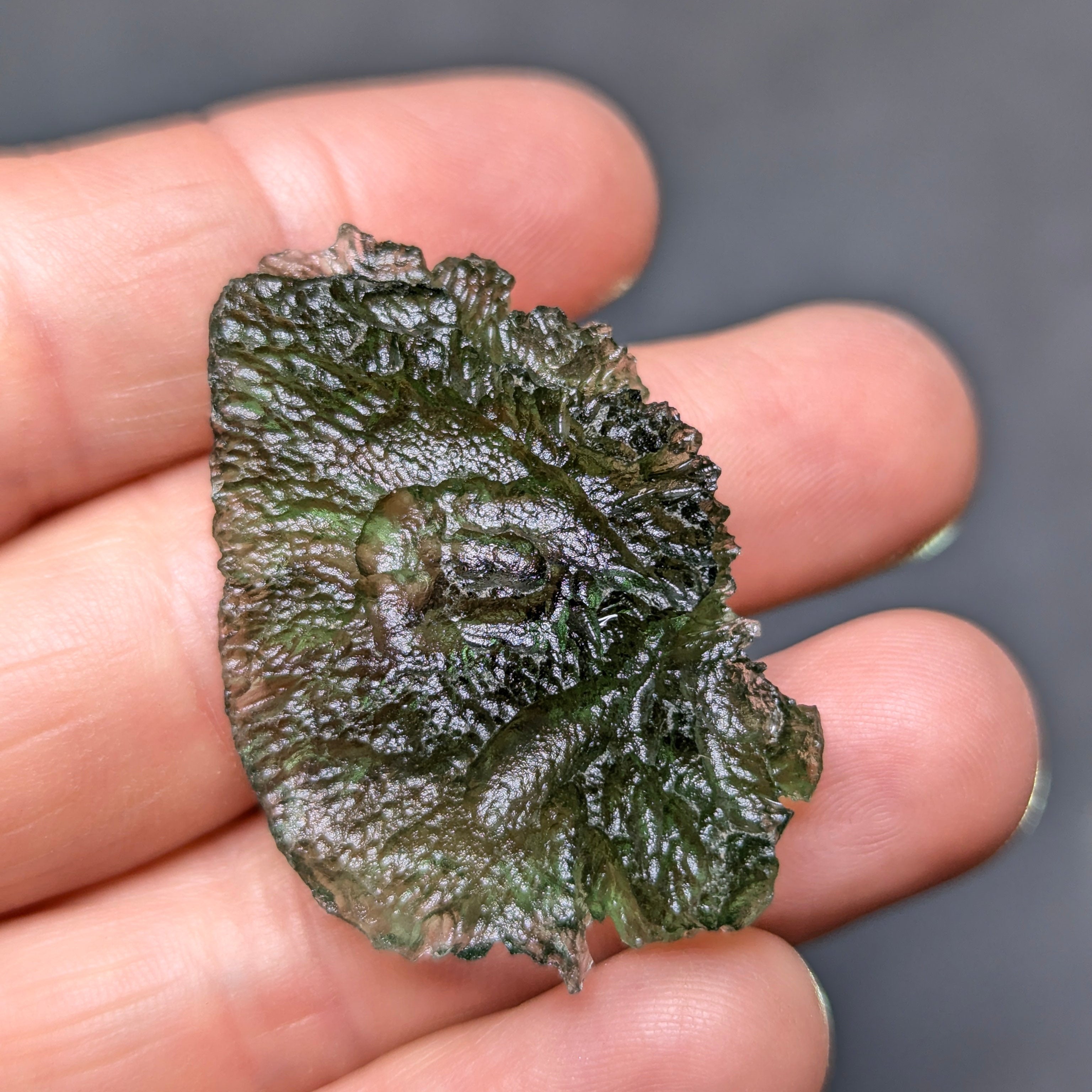 Natural Moldavite from the Olešnice locality with electrifying neon green color, glossy luster, deep grooves and vivid green translucency under illumination in hand - back view.