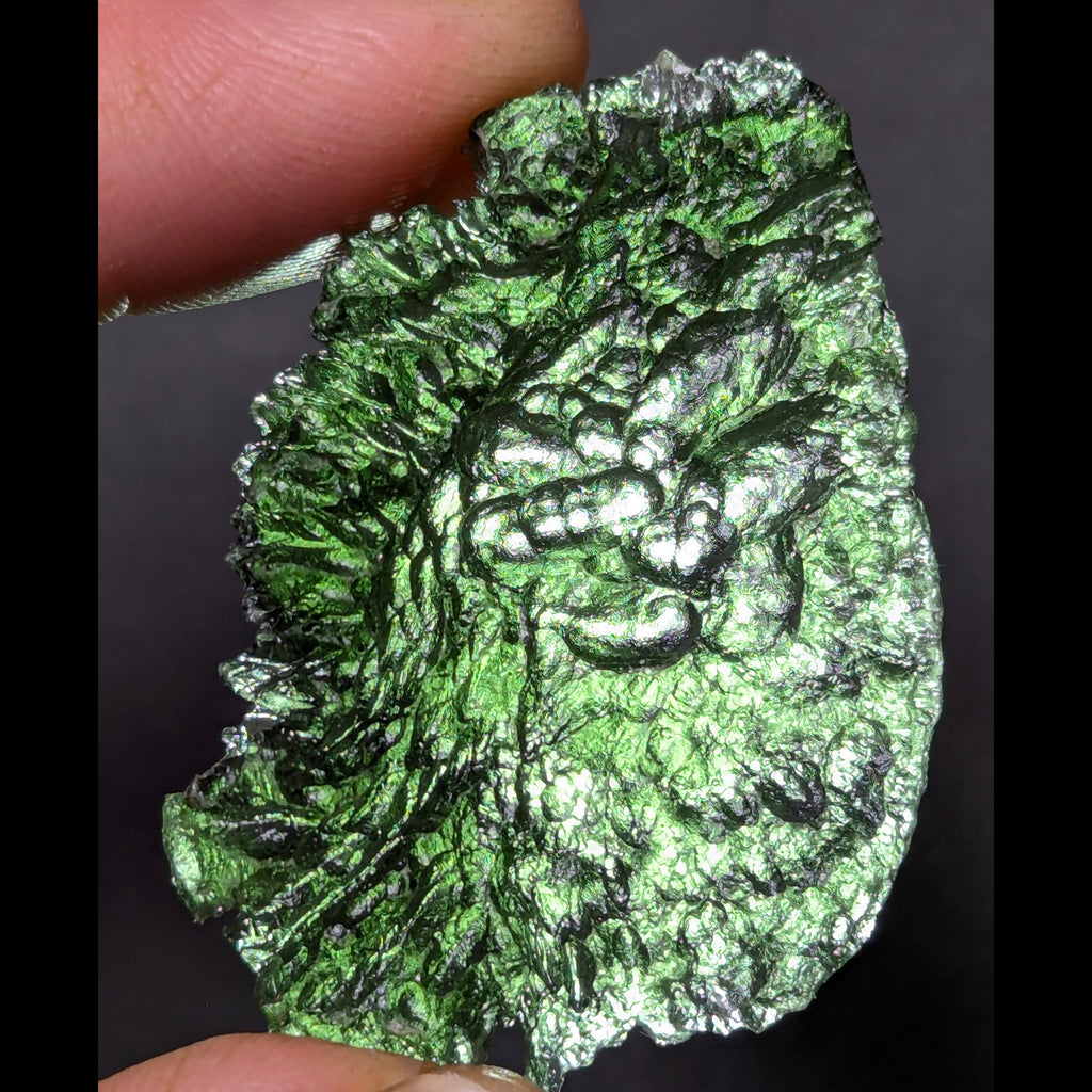 Natural Moldavite from the Olešnice locality with electrifying neon green color, glossy luster, deep grooves and vivid green translucency under illumination in hand - front view, backlight.