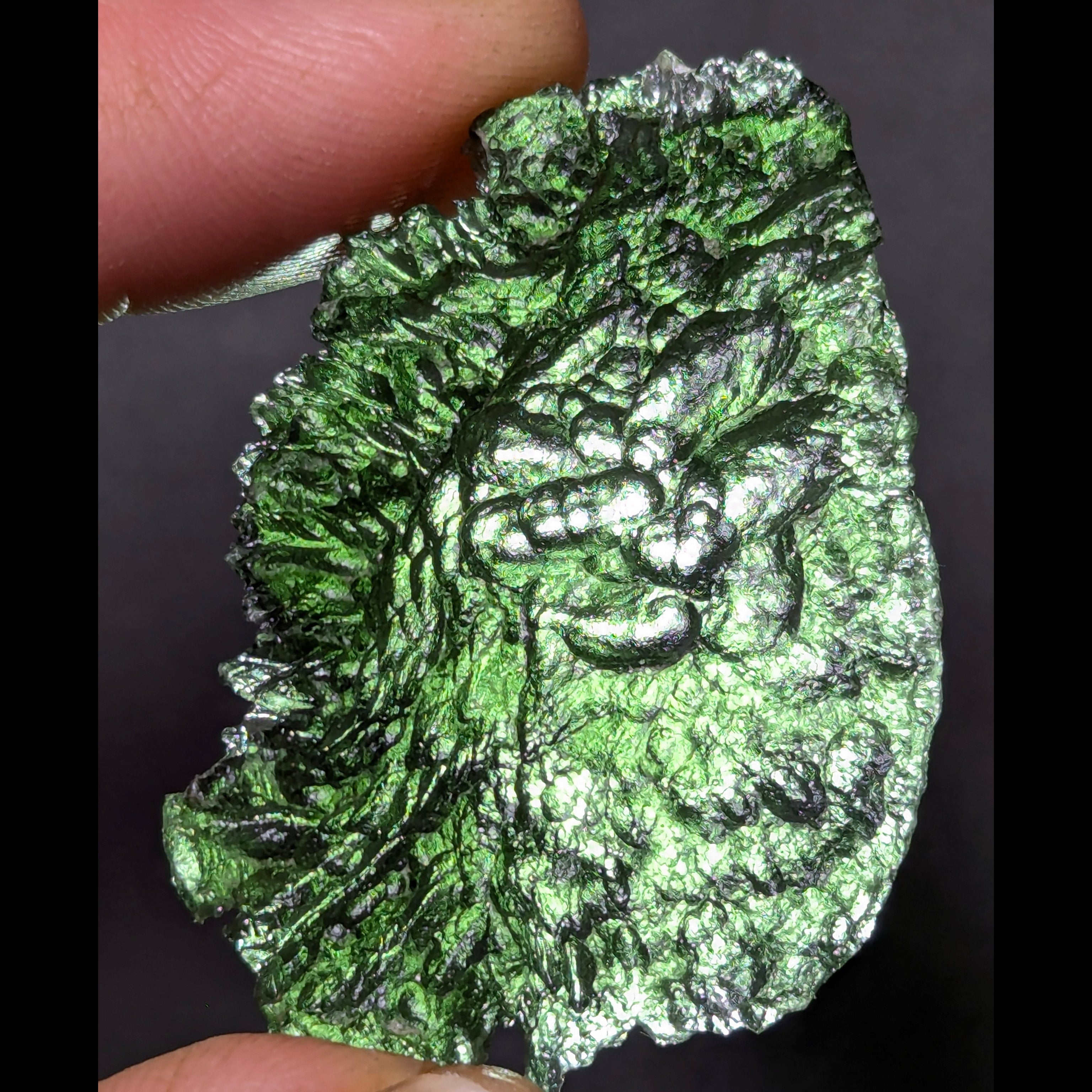 Natural Moldavite from the Olešnice locality with electrifying neon green color, glossy luster, deep grooves and vivid green translucency under illumination in hand - front view, backlight.