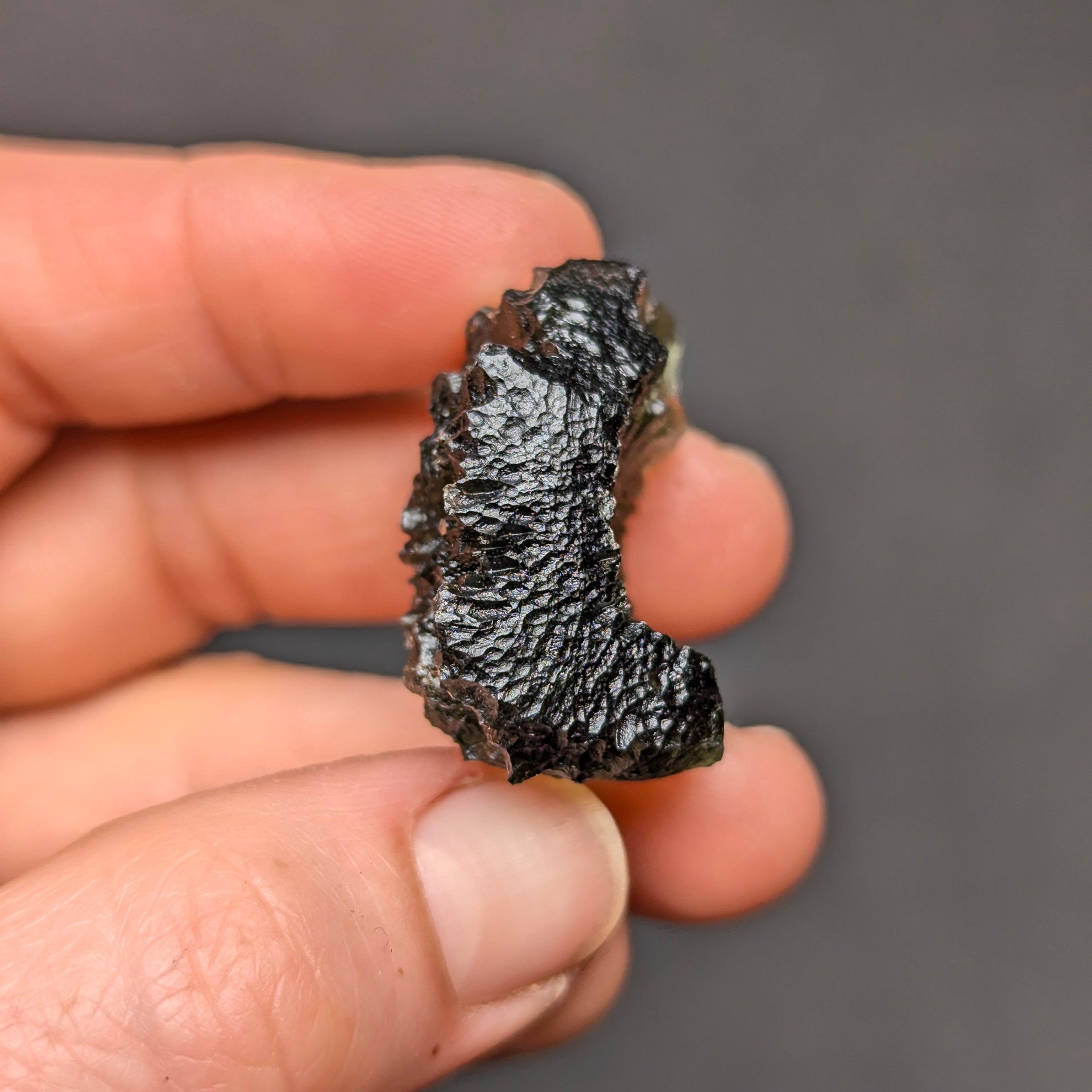 Natural Olešnice 13.87 g moldavite with deep sculpted texture and vivid green translucency under transmitted light - side view.