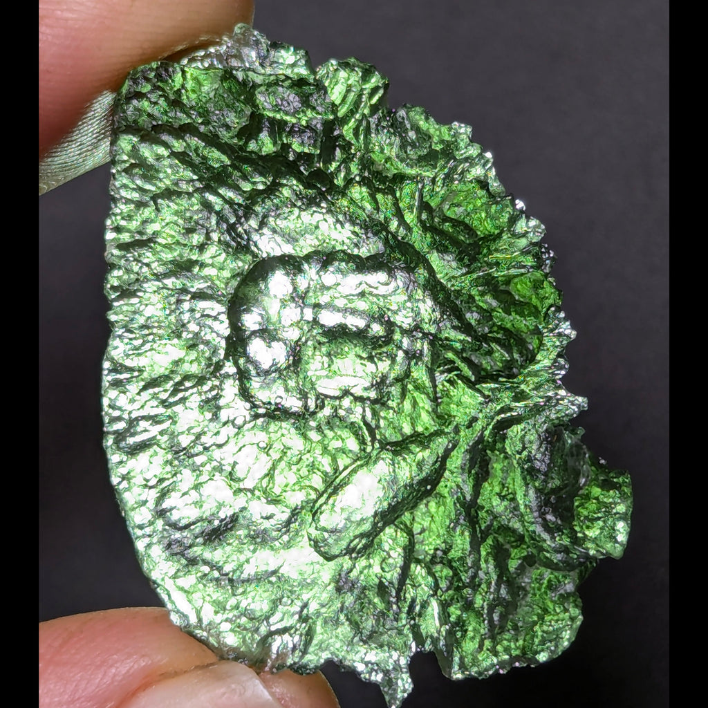 Natural Moldavite from the Olešnice locality with electrifying neon green color, glossy luster, deep grooves and vivid green translucency under illumination in hand - back side, backlight.