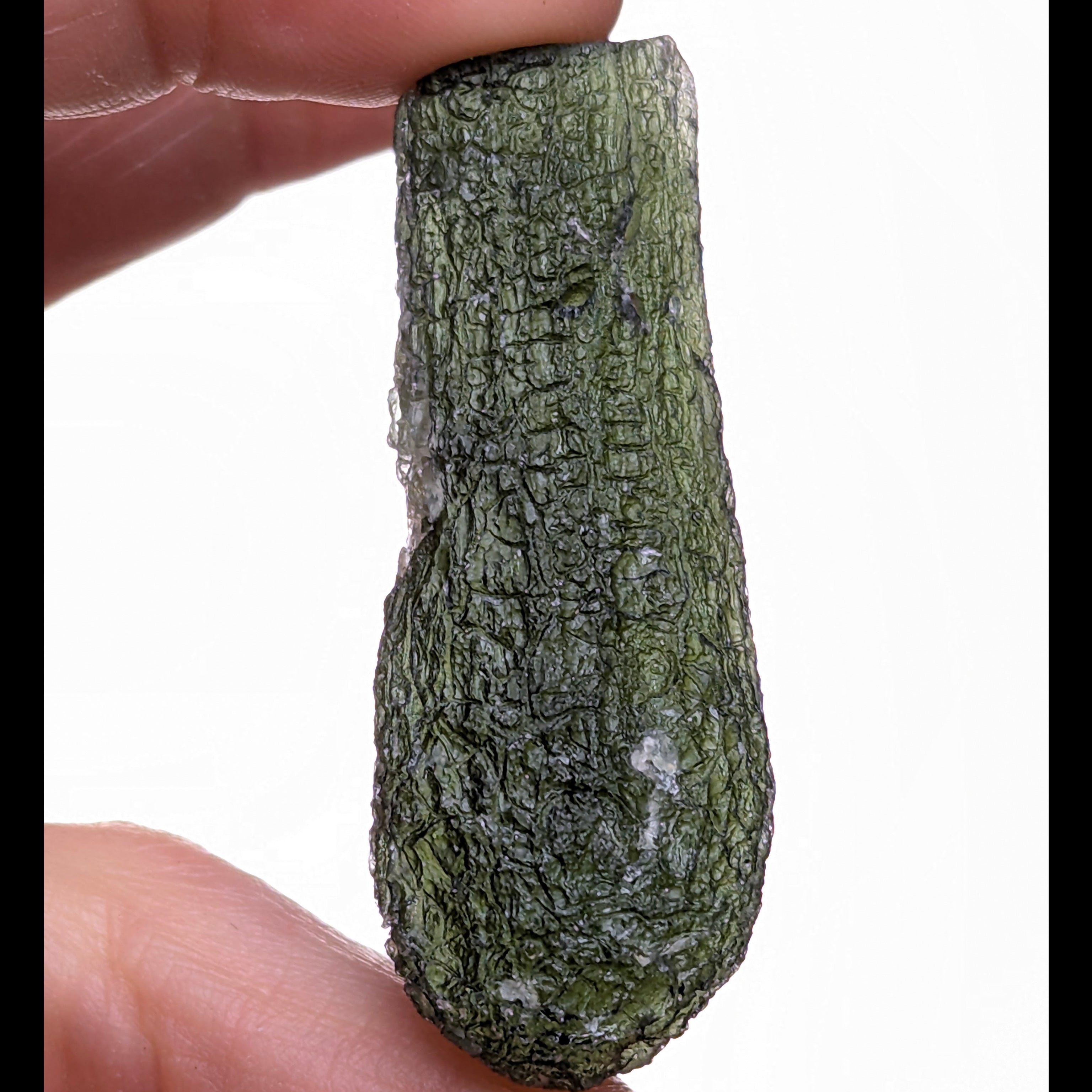 Natural Moldavite from the Jankov locality in hand, front view with elongated drop-like shape, tree bark sculpture, dark olive green translucency and authentic natural relief. Weight 15.62 g - front side, white background.