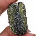 Natural Moldavite from the Olešnice locality with dramatic sculpture, deep central groove, naturally opened bubbles and vivid green translucency under illumination in hand - front view.