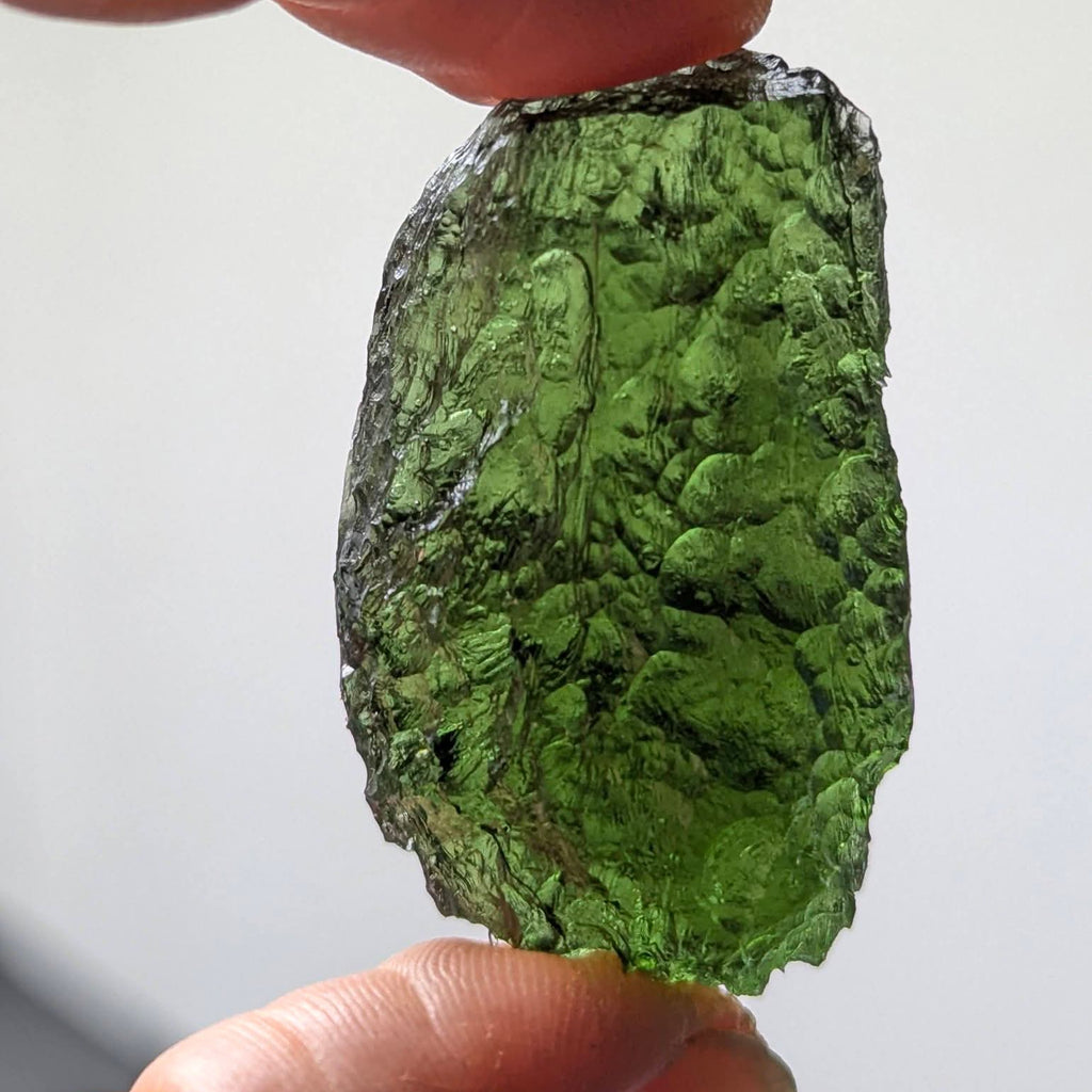 Natural Moldavite from the Krasejovka locality on white background with glossy lacquer-like surface, deep sculpture, pronounced grooves, vivid green translucency and authentic natural relief. Weight 14 g - back side, daylight.