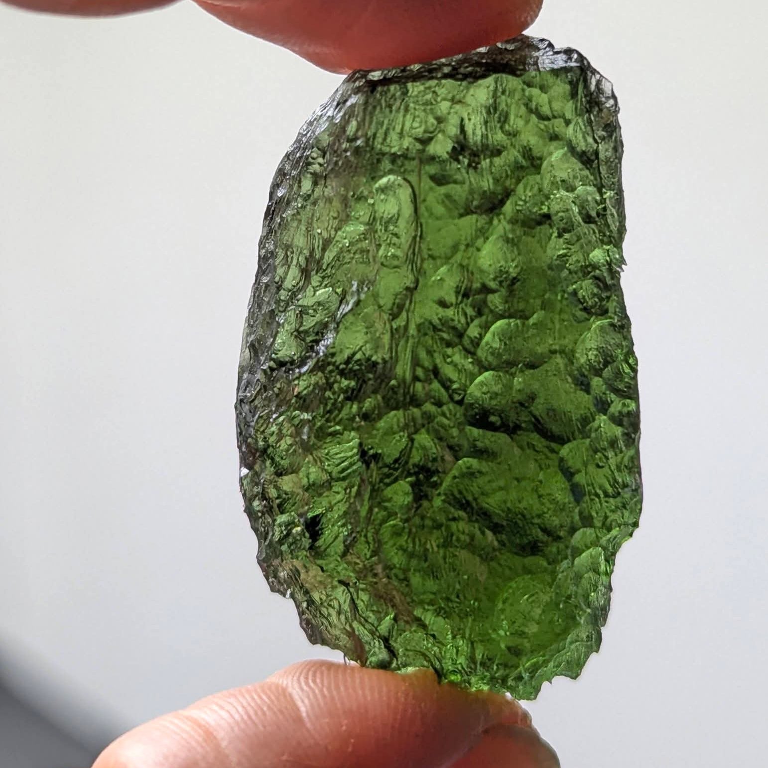 Natural Moldavite from the Krasejovka locality on white background with glossy lacquer-like surface, deep sculpture, pronounced grooves, vivid green translucency and authentic natural relief. Weight 14 g - back side, daylight.